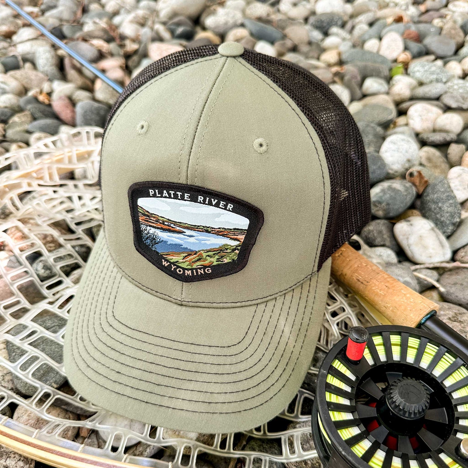 A green structured trucker hat with a patch on the front showing a hand-drawn image of a section of the North Platte River in Wyoming.